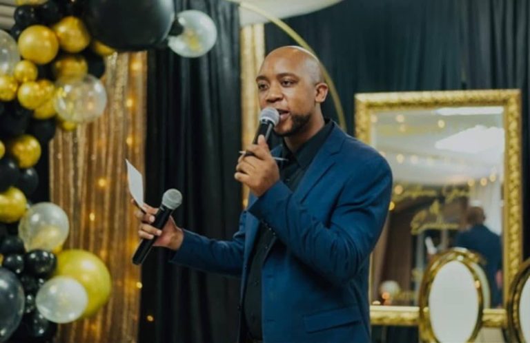 Shozi The Emcee in a blue suit speaking into a microphone at a black and gold themed party with balloon decor