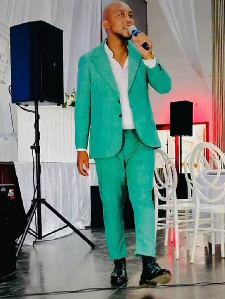 Shozi The Emcee in a bright green suit holding a microphone on stage at a white draped reception venue